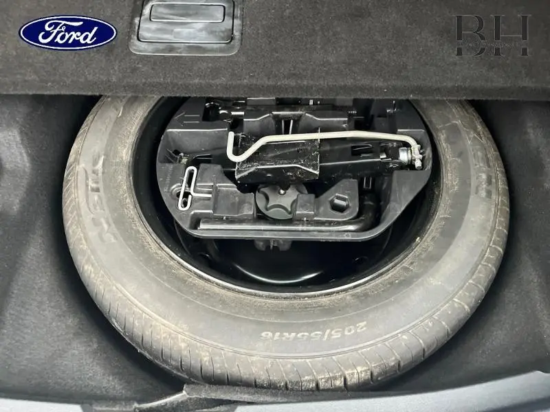 Gros plan sur la roue de secours et le cric dans le coffre d'une Renault Mégane Break gris platine, vue de dessus.