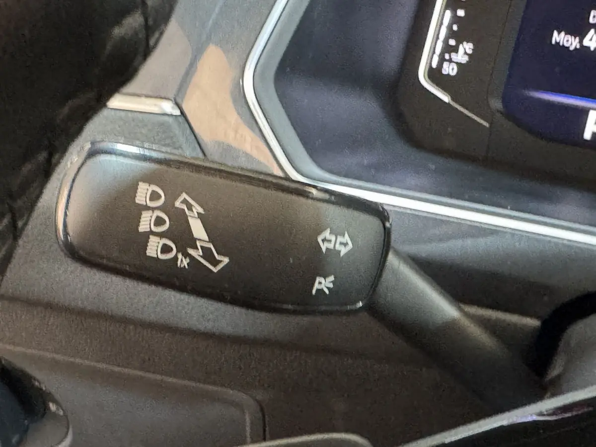 Gros plan sur la manette de clignotants noire à gauche du volant du Volkswagen Tiguan Allspace gris foncé, avec pictogrammes blancs.