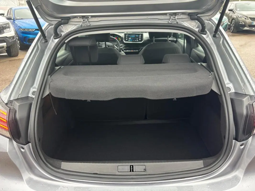 Coffre ouvert d'une Peugeot 208 Hybrid 100 e-DCS6 Style gris, vue arrière avec intérieur et écran tactile visibles.