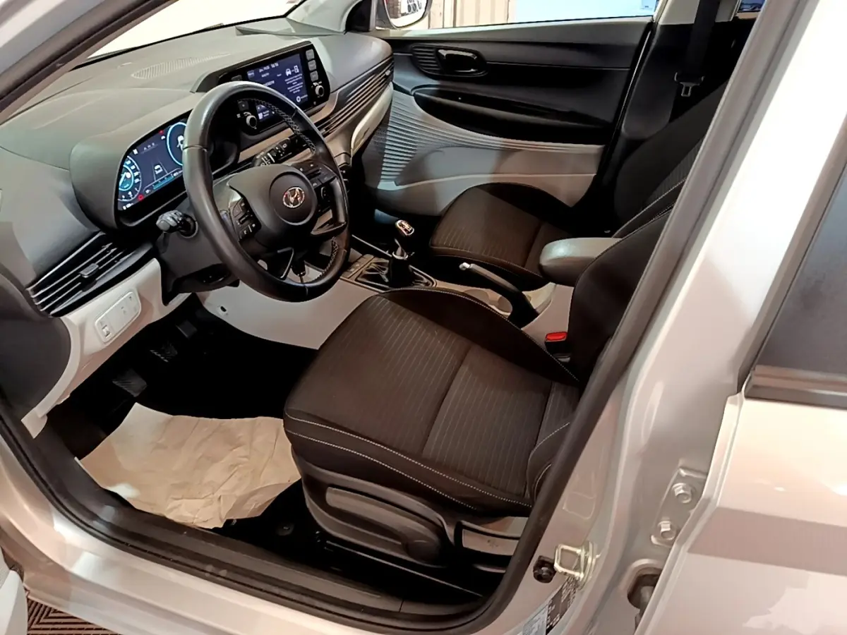 Vue intérieure côté conducteur de la Hyundai i20 gris clair 2022, volant cuir multifonctions et tableau de bord digital.