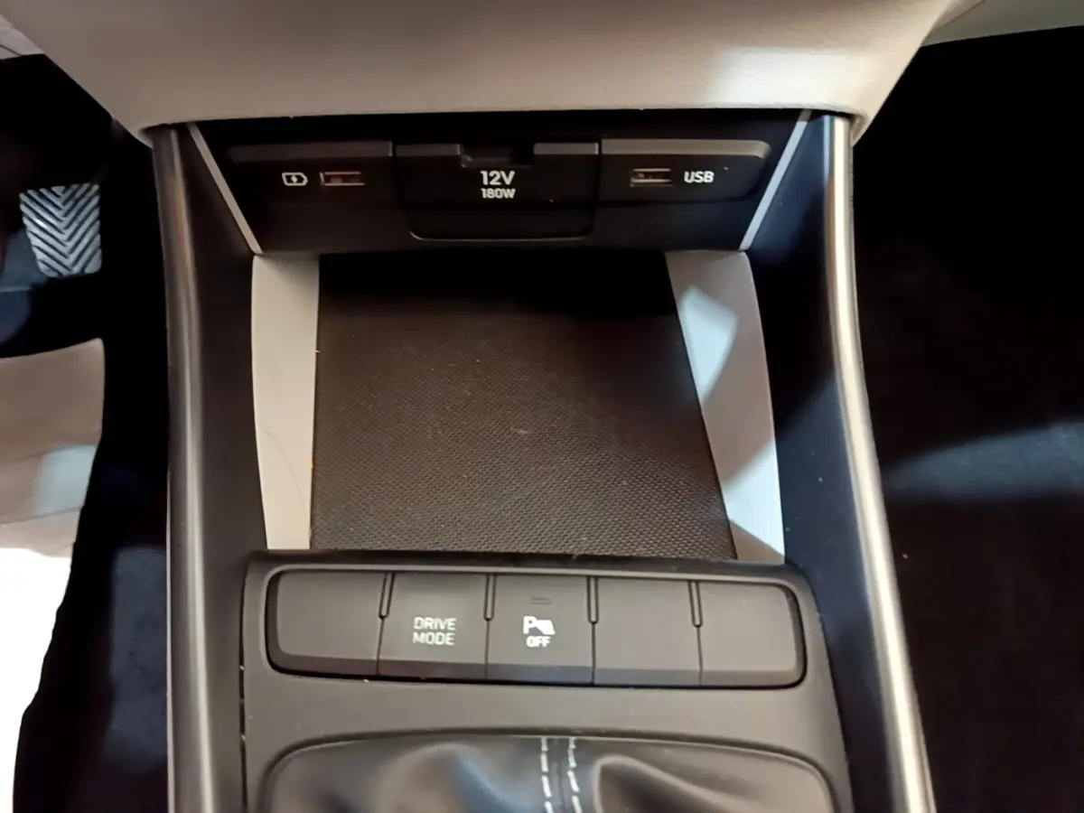 Gros plan sur la console centrale noire du Hyundai i20 2022, montrant prises USB, prise 12V et boutons de contrôle.