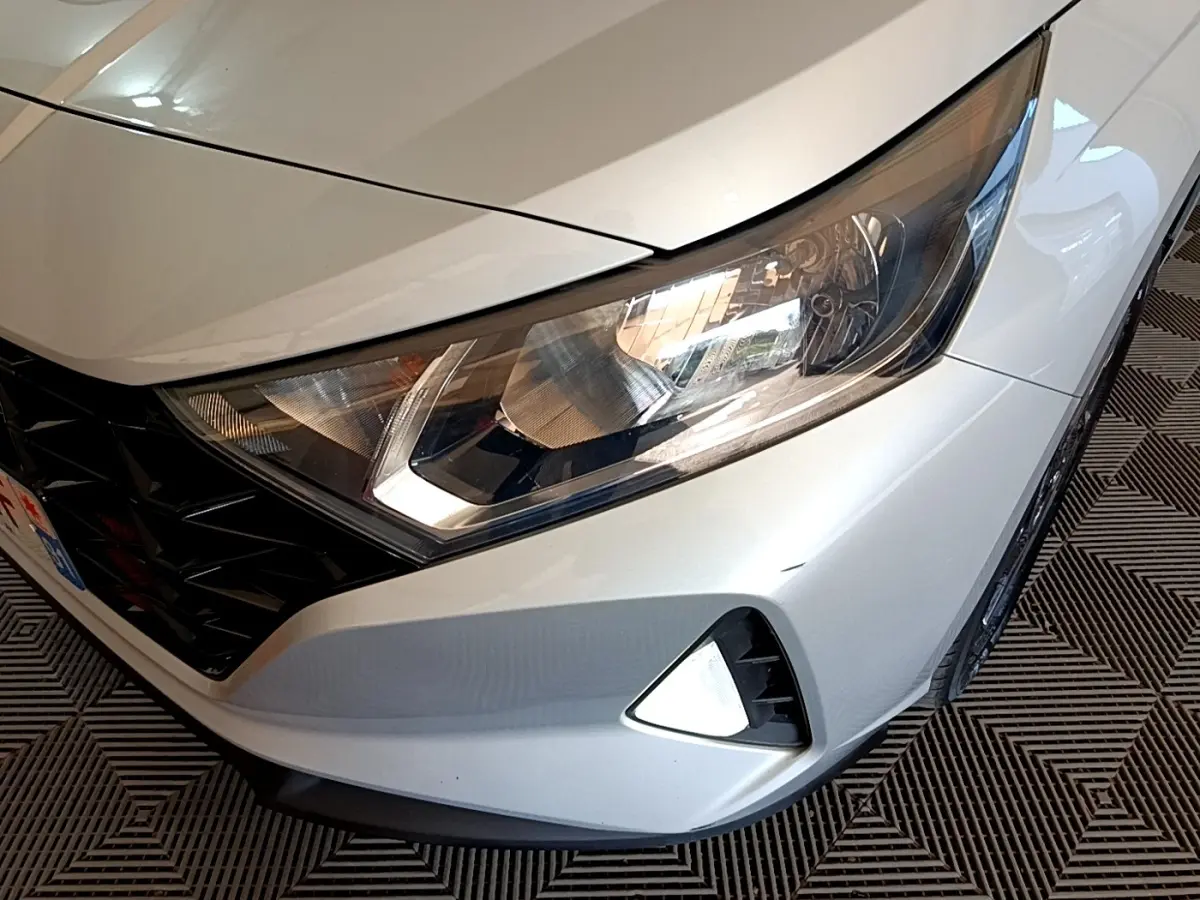 Gros plan sur l'avant droit gris clair de la Hyundai i20 2022 avec phare et calandre noire en losange.