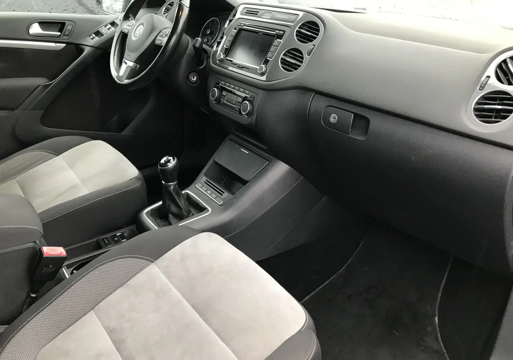 Intérieur avant du Volkswagen Tiguan Sportline 2012, vue côté passager avec sièges tissu gris clair et volant multifonctions noir.