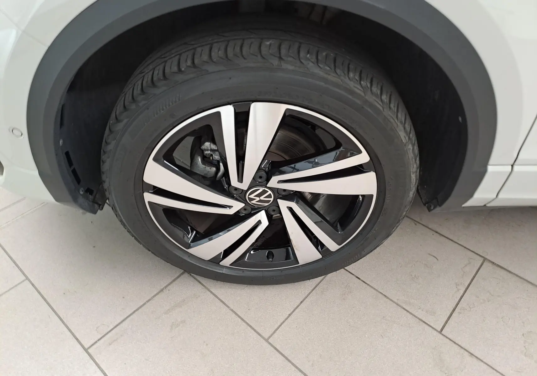 Gros plan sur la roue avant gauche du Volkswagen T-Roc 2024 Gris Ascot avec jante alliage R-Line bicolore.