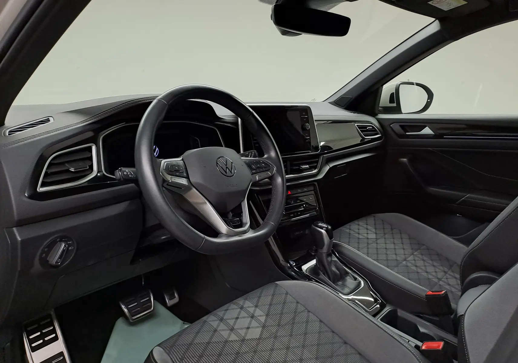 Intérieur du Volkswagen T-Roc 2024 vu côté conducteur, avec volant multifonction et sièges tissu noir à motifs.