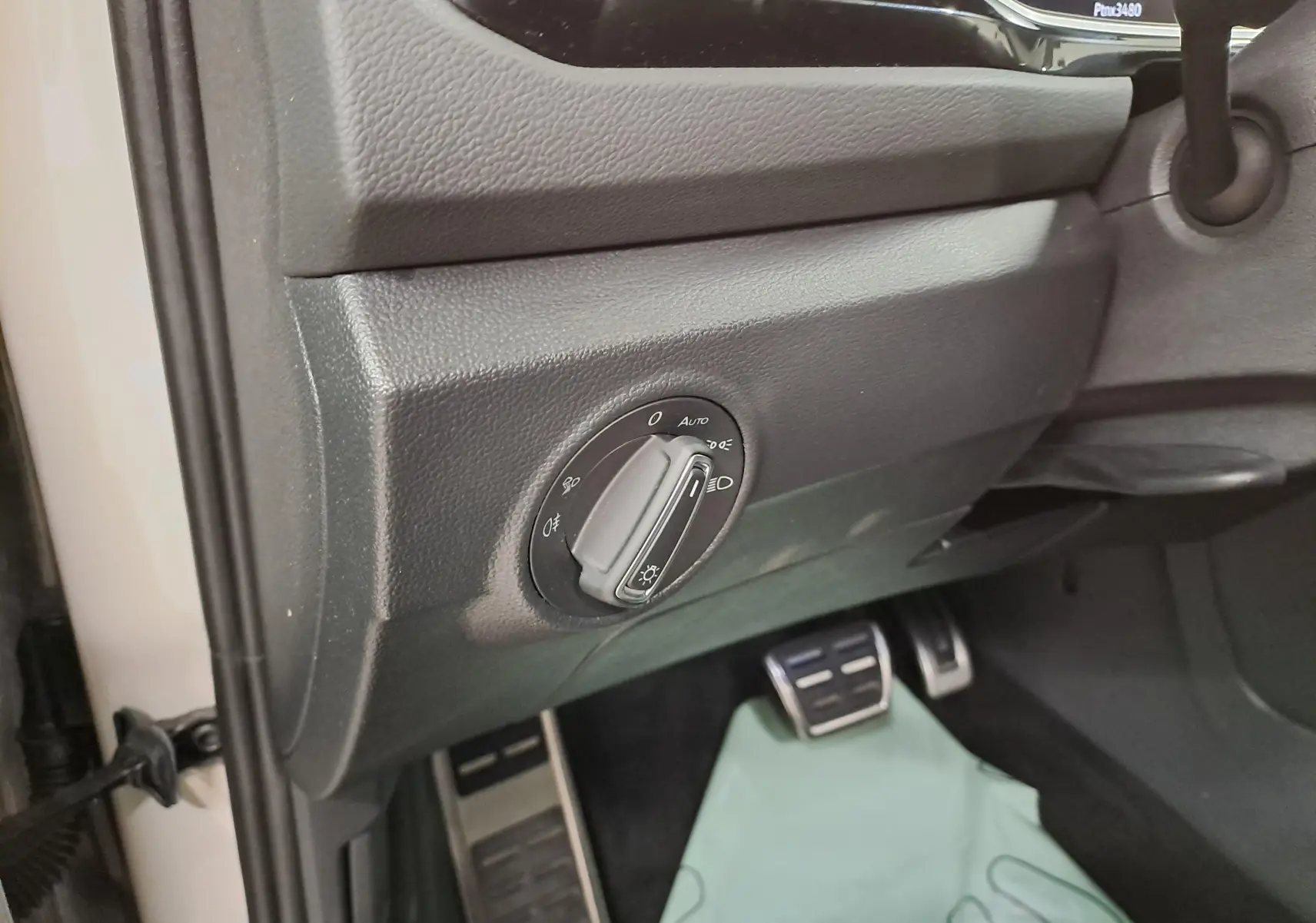 Gros plan sur le bouton des phares et les pédales côté conducteur d'un Volkswagen T-Roc 1.5 TSI R-Line gris Ascot 2024.