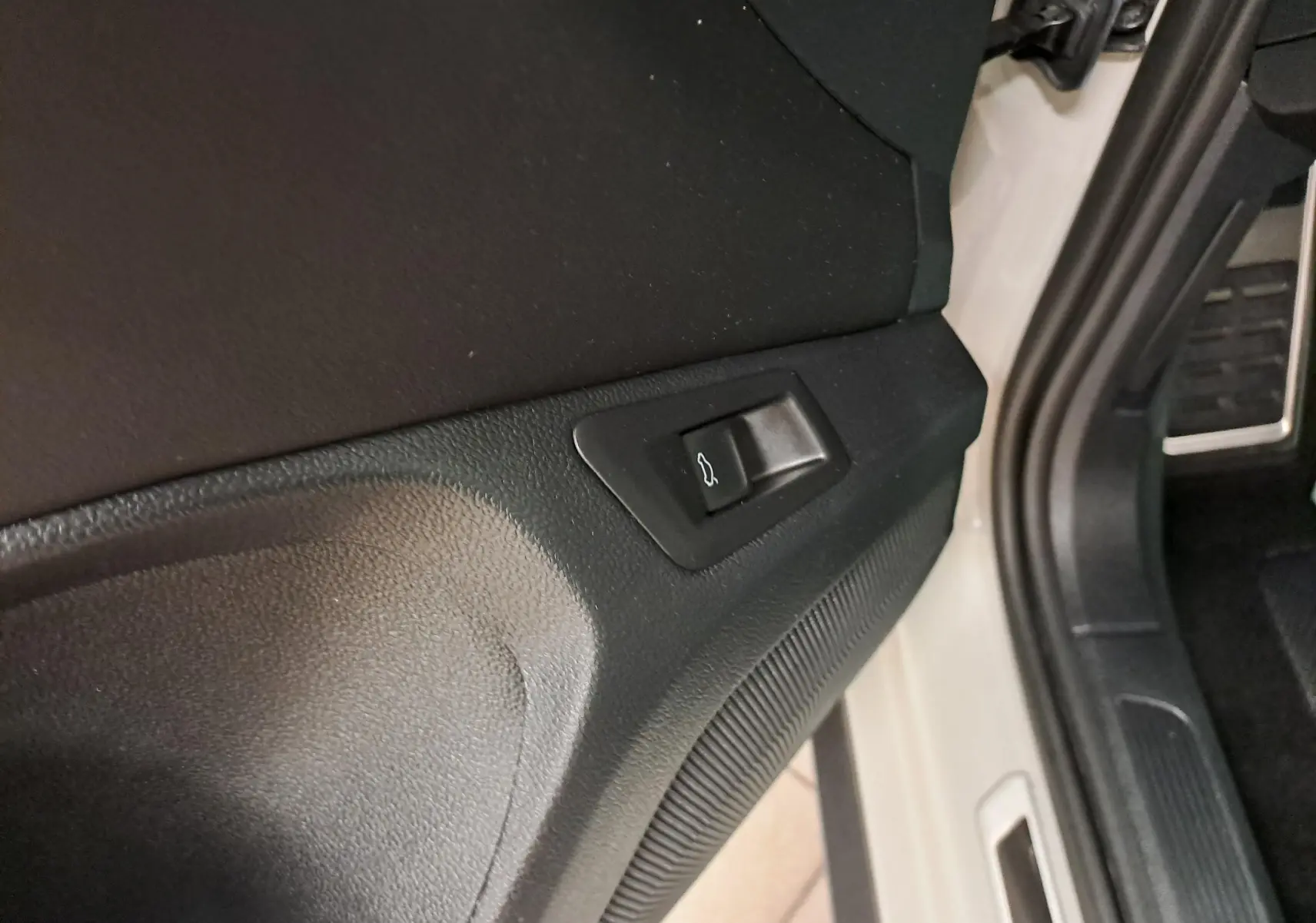 Bouton d'ouverture du coffre sur la garniture intérieure côté conducteur du Volkswagen T-Roc Gris Ascot 2024.