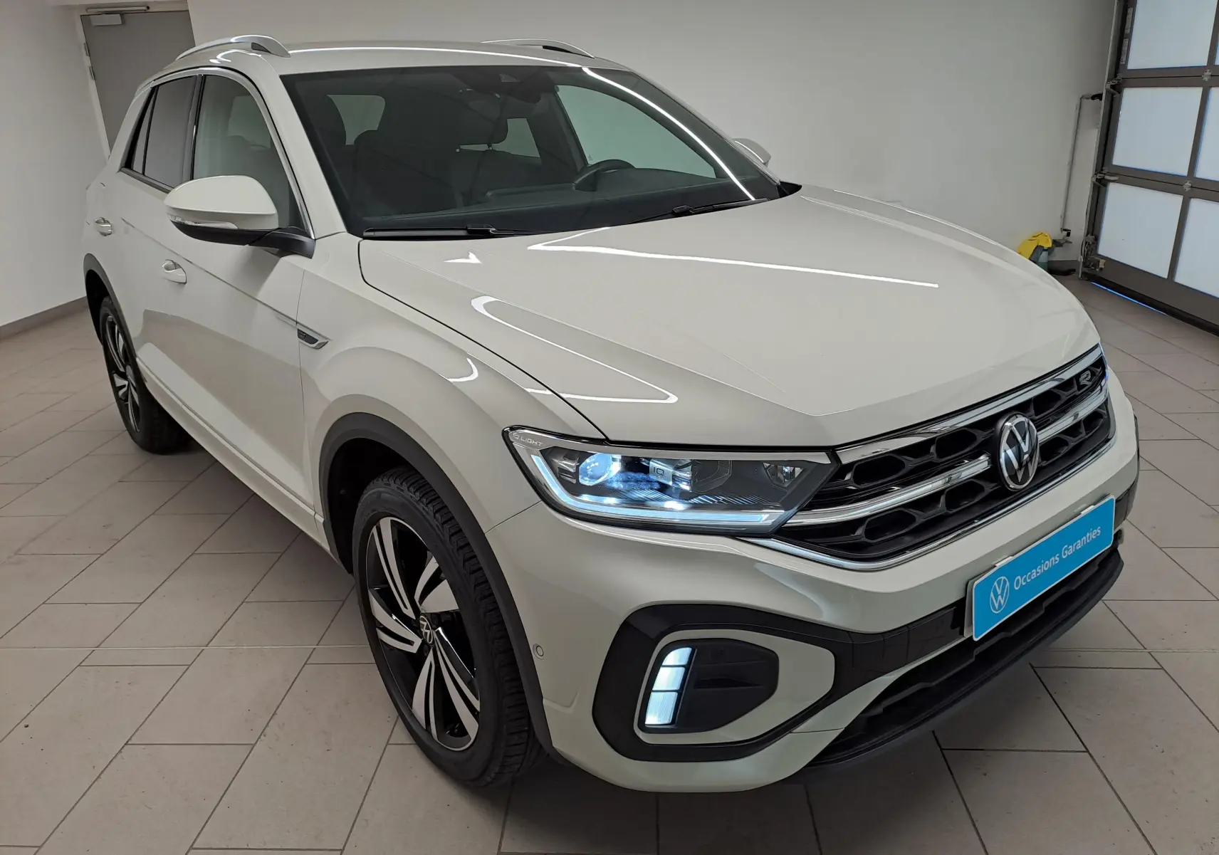 Volkswagen T-Roc 1.5 TSI R-Line gris Ascot vu de 3/4 avant droit avec feux LED allumés en intérieur.