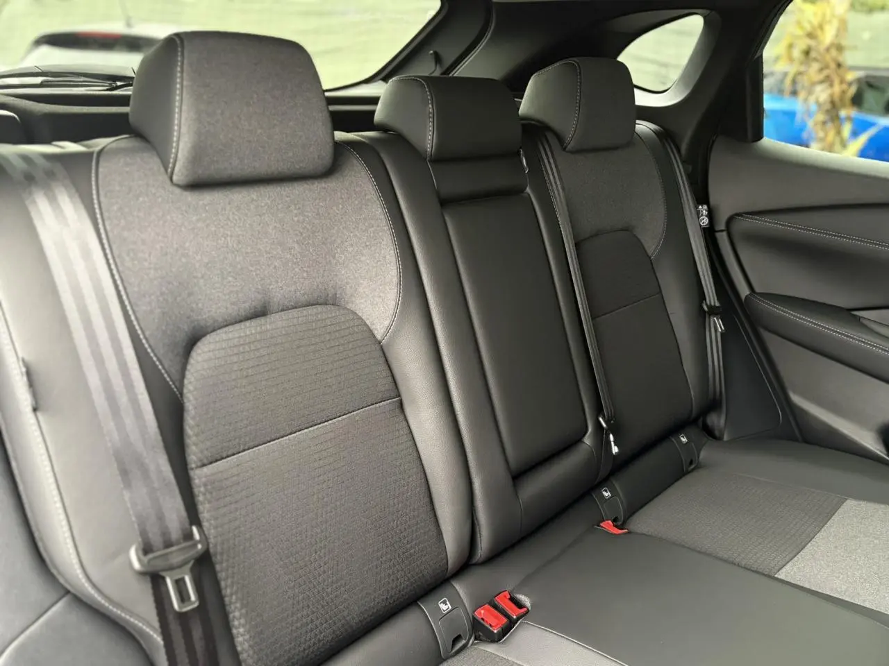 Vue latérale intérieure des sièges arrière gris et noirs du Nissan Qashqai 2024 avec ceintures de sécurité visibles.