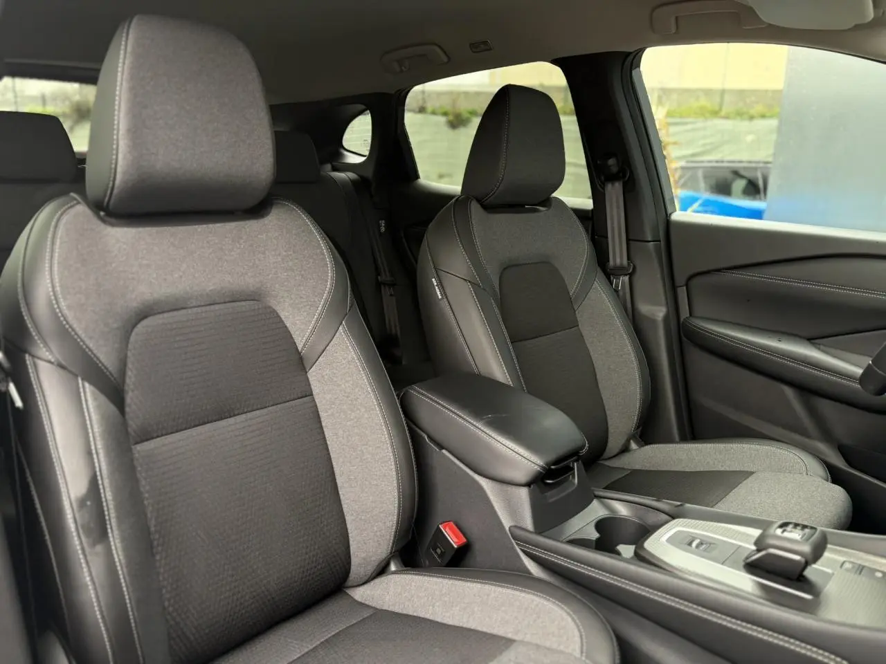 Vue intérieure des sièges avant gris clair et foncé du Nissan Qashqai 2024 avec accoudoir central et console moderne.