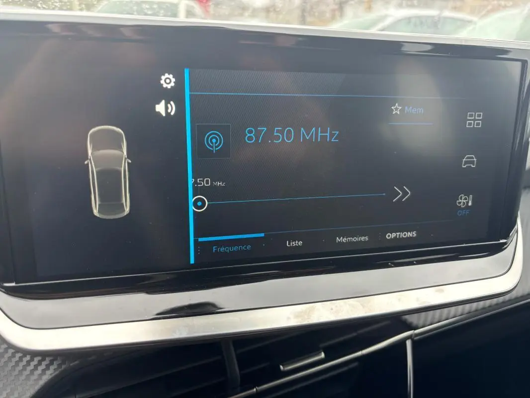 Écran tactile central affichant la radio à 87,50 MHz dans l’habitacle du Peugeot 208 gris, version Hybrid 100 e-DCS6 Style.