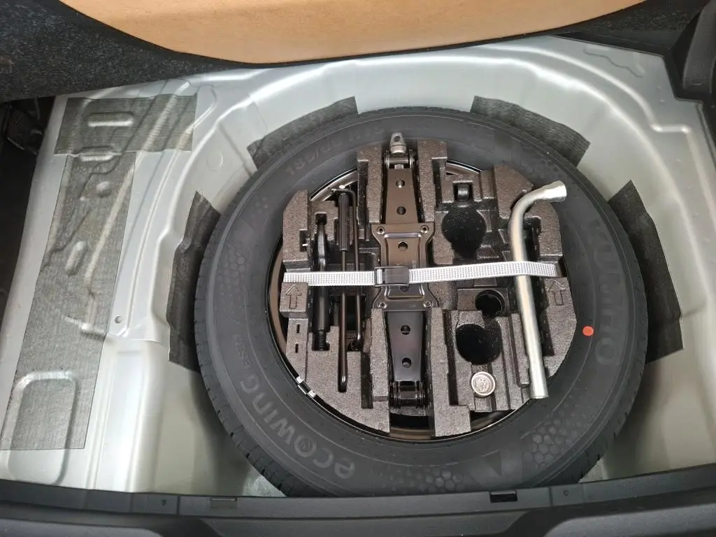 Vue plongeante sur la roue de secours grise avec outils de bord dans le coffre d'une Skoda Fabia Ambition 2023.