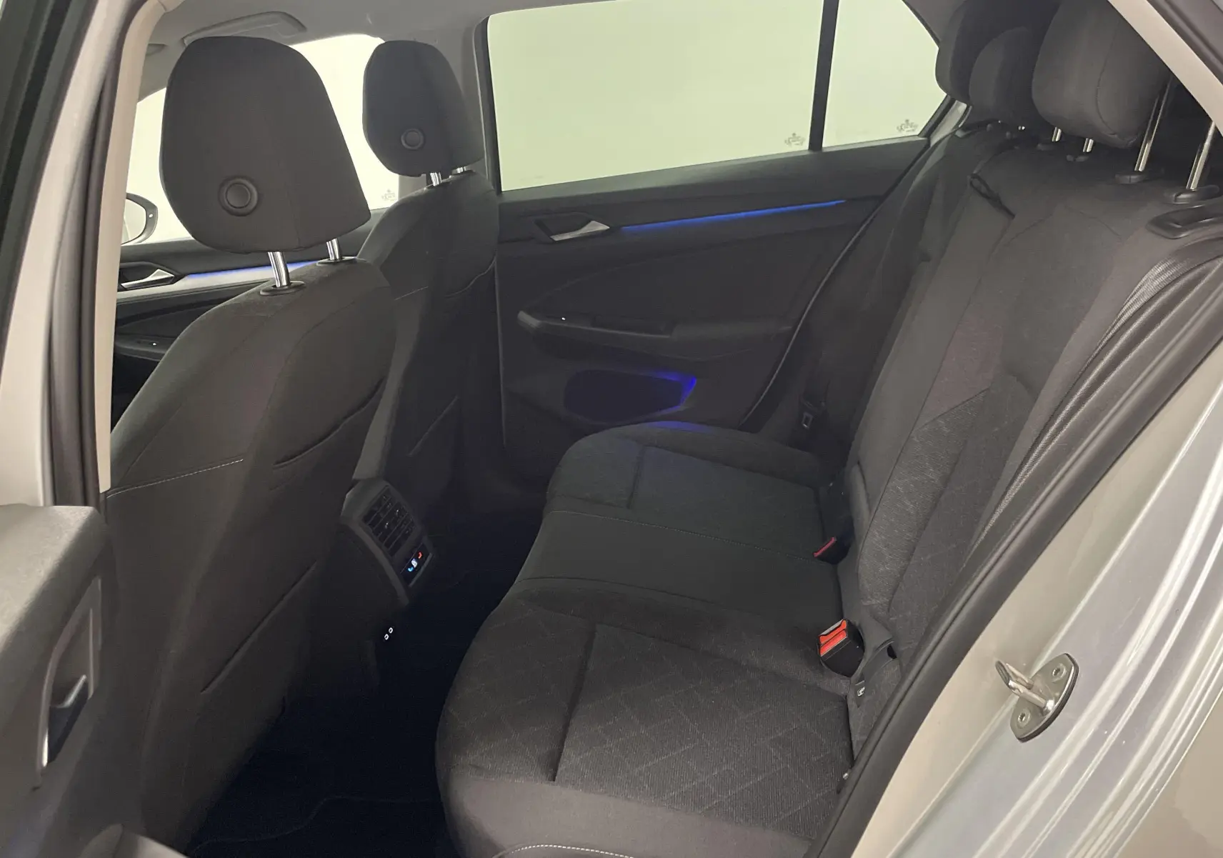 Vue intérieure arrière droite d'une Volkswagen Golf 2.0 TDI 115 argent avec sièges tissu noir et éclairage d'ambiance bleu.