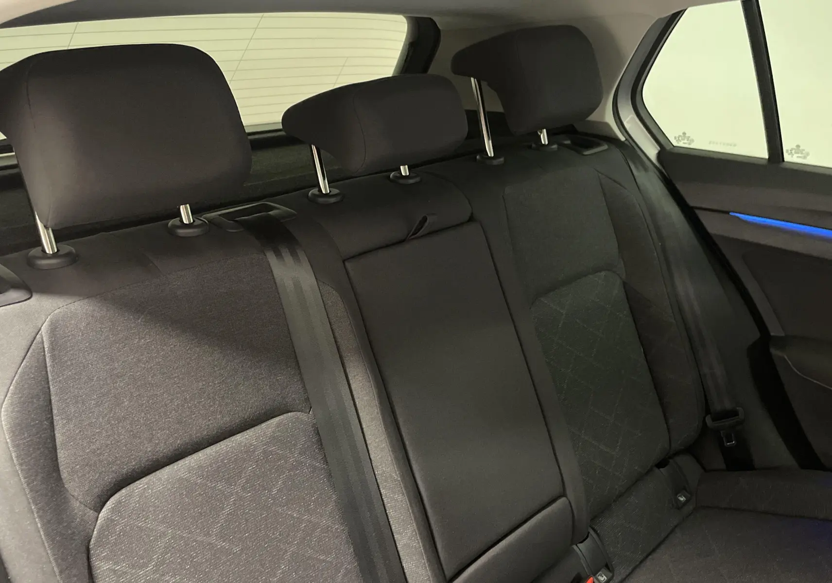 Vue intérieure des sièges arrière noirs de la Volkswagen Golf 2.0 TDI 115 DSG7 avec éclairage d'ambiance bleu sur la porte.