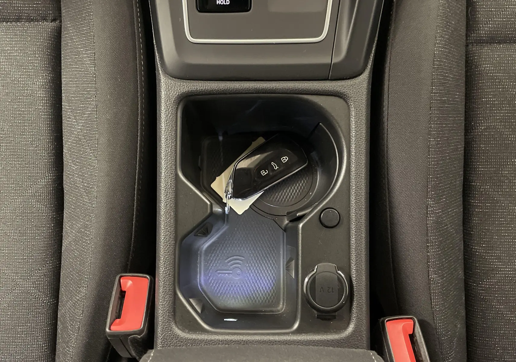 Gros plan sur la console centrale noire d'une Volkswagen Golf 2022 avec clé et prise 12V visible entre les sièges.