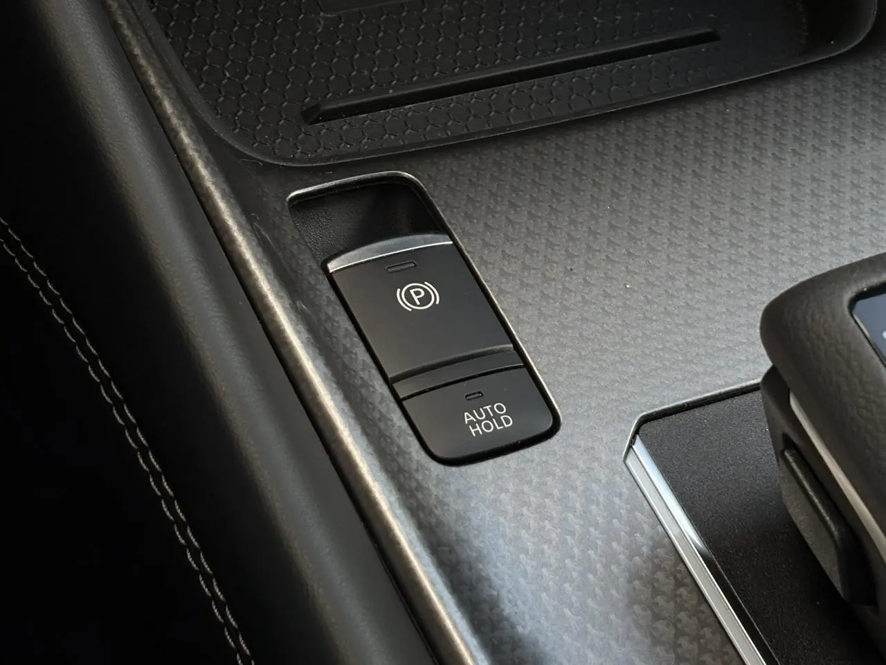Gros plan sur la console centrale du Nissan Qashqai 2025, montrant les boutons du frein à main électrique et Auto Hold.
