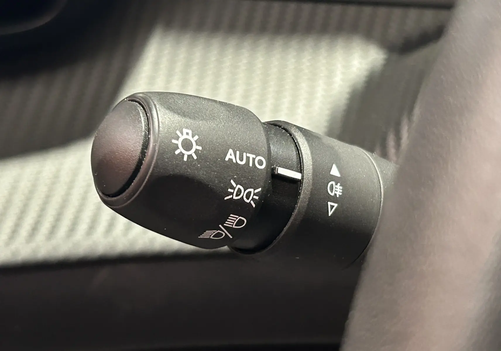 Gros plan sur la commande des phares avec réglage automatique dans l'habitacle d'une Peugeot 208 2025.
