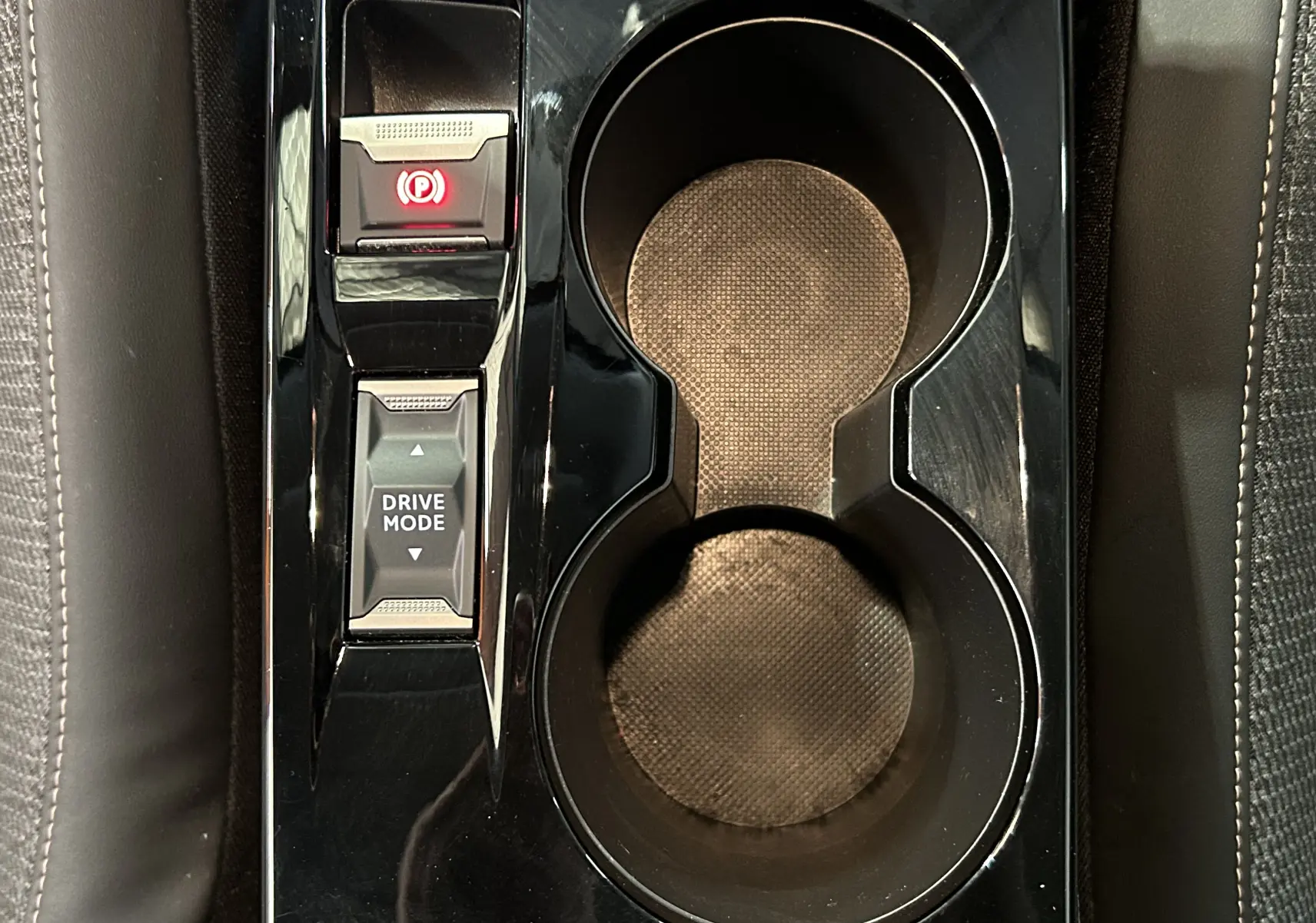 Gros plan sur la console centrale noire brillante de la Peugeot 208 avec porte-gobelets et bouton Drive Mode.