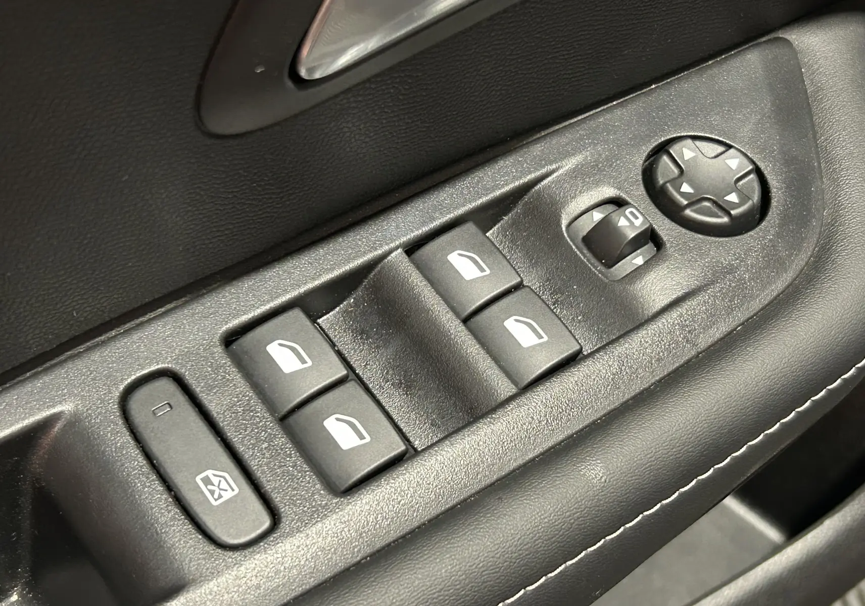 Gros plan sur les commandes de lève-vitres et réglage des rétroviseurs intérieurs noirs d'une Peugeot 208 2025.