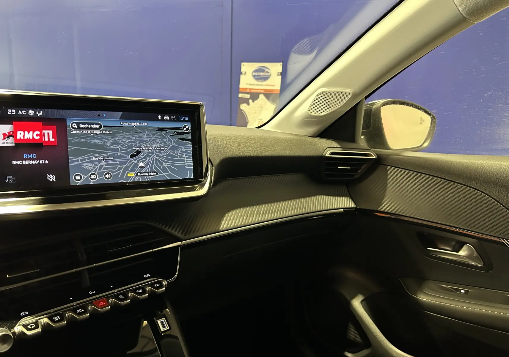 Vue intérieure côté passager de la Peugeot 208 2025 avec écran GPS et finition carbone sur tableau de bord.