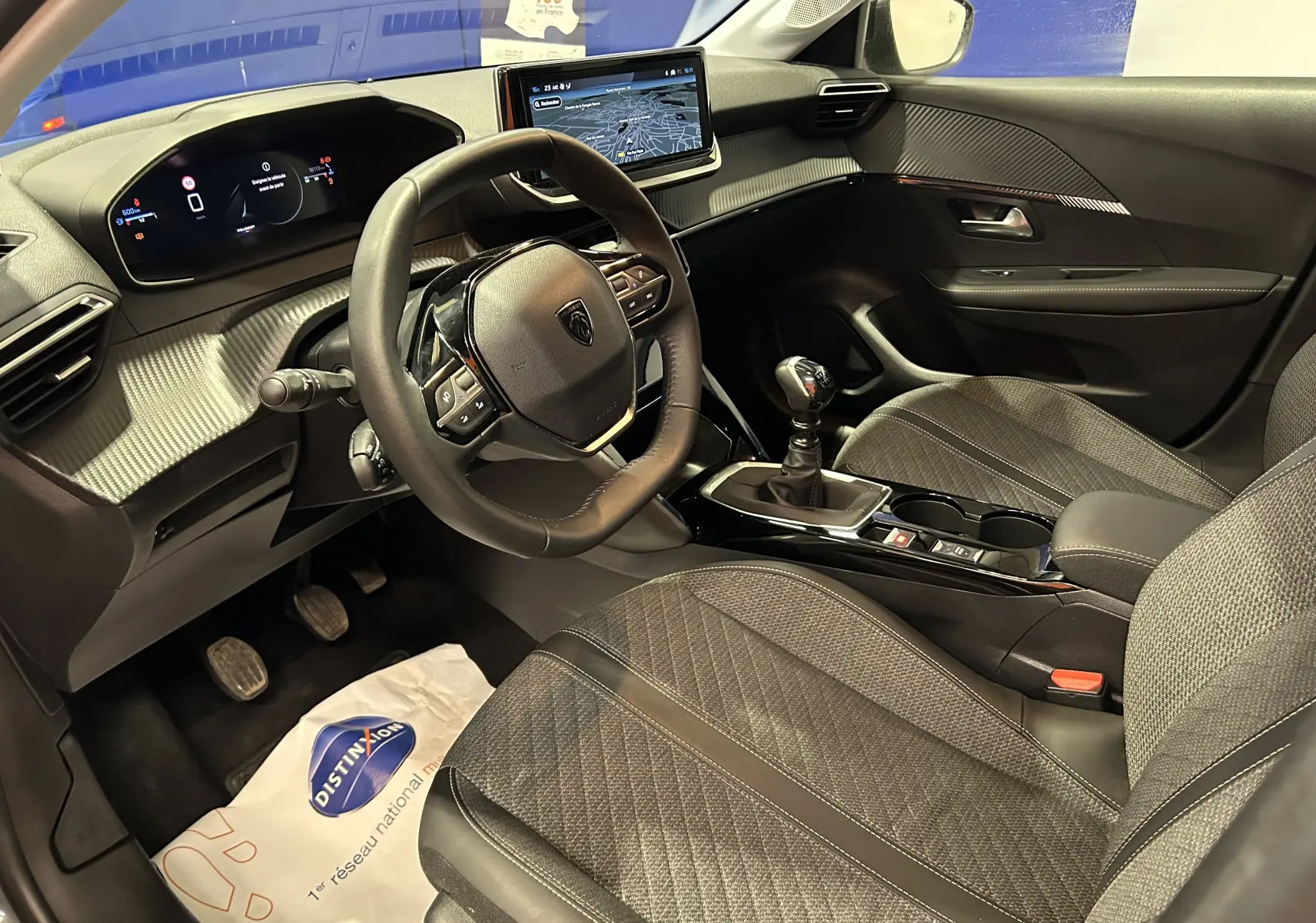 Vue intérieure côté conducteur de la Peugeot 208 2025 avec volant compact, écran GPS et levier de vitesse manuel.