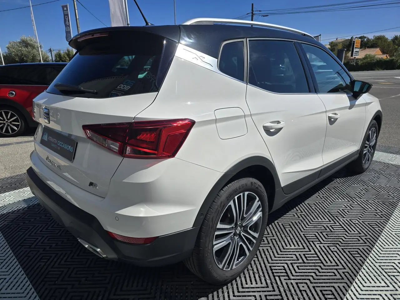 Vue 3/4 arrière droite d'un SEAT Arona blanc avec toit noir et jantes alliage, en extérieur sur parking.