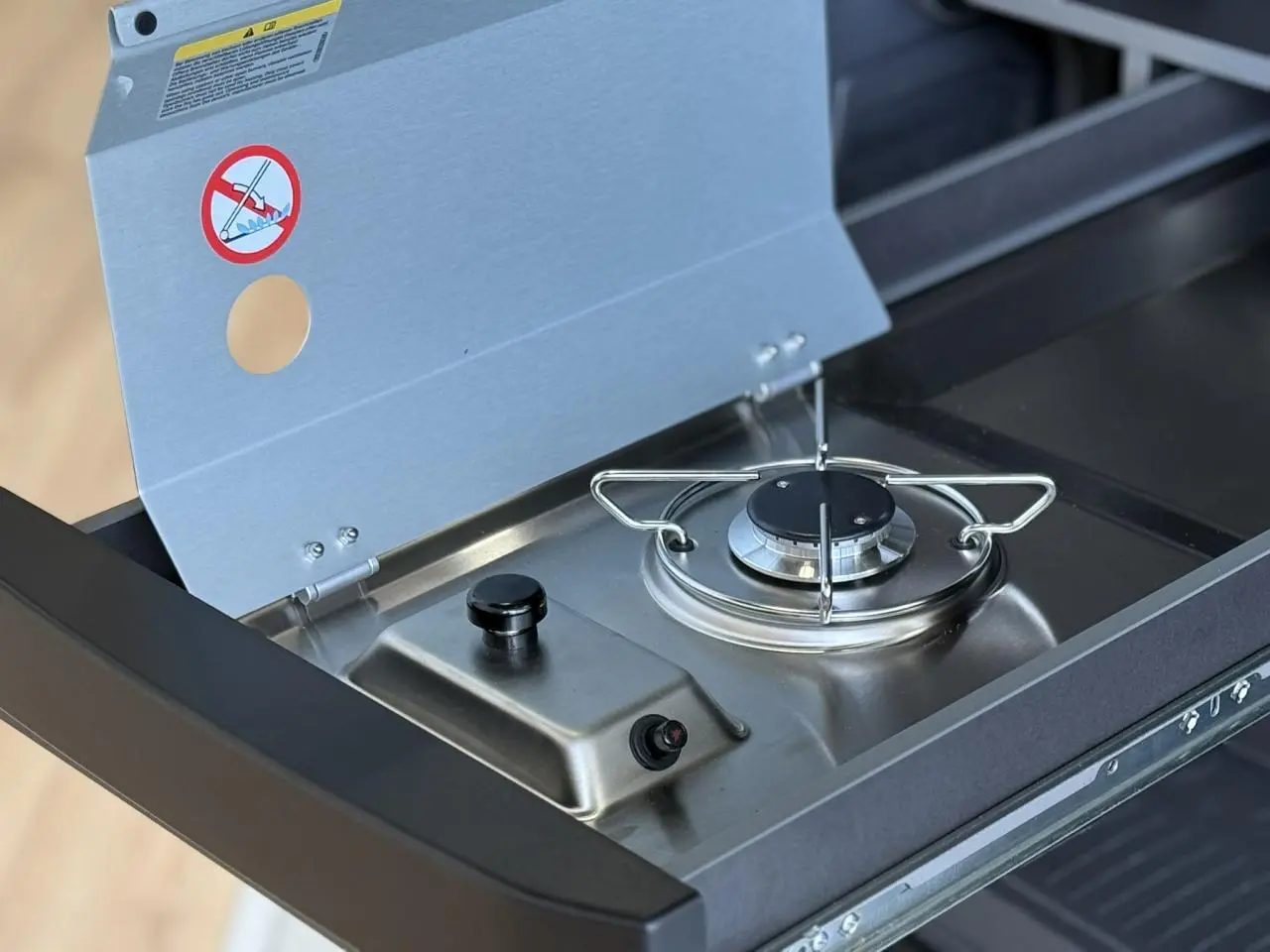 Gros plan sur le réchaud à gaz extensible en inox de la mini-cuisine du Volkswagen California T7 blanc Candy.