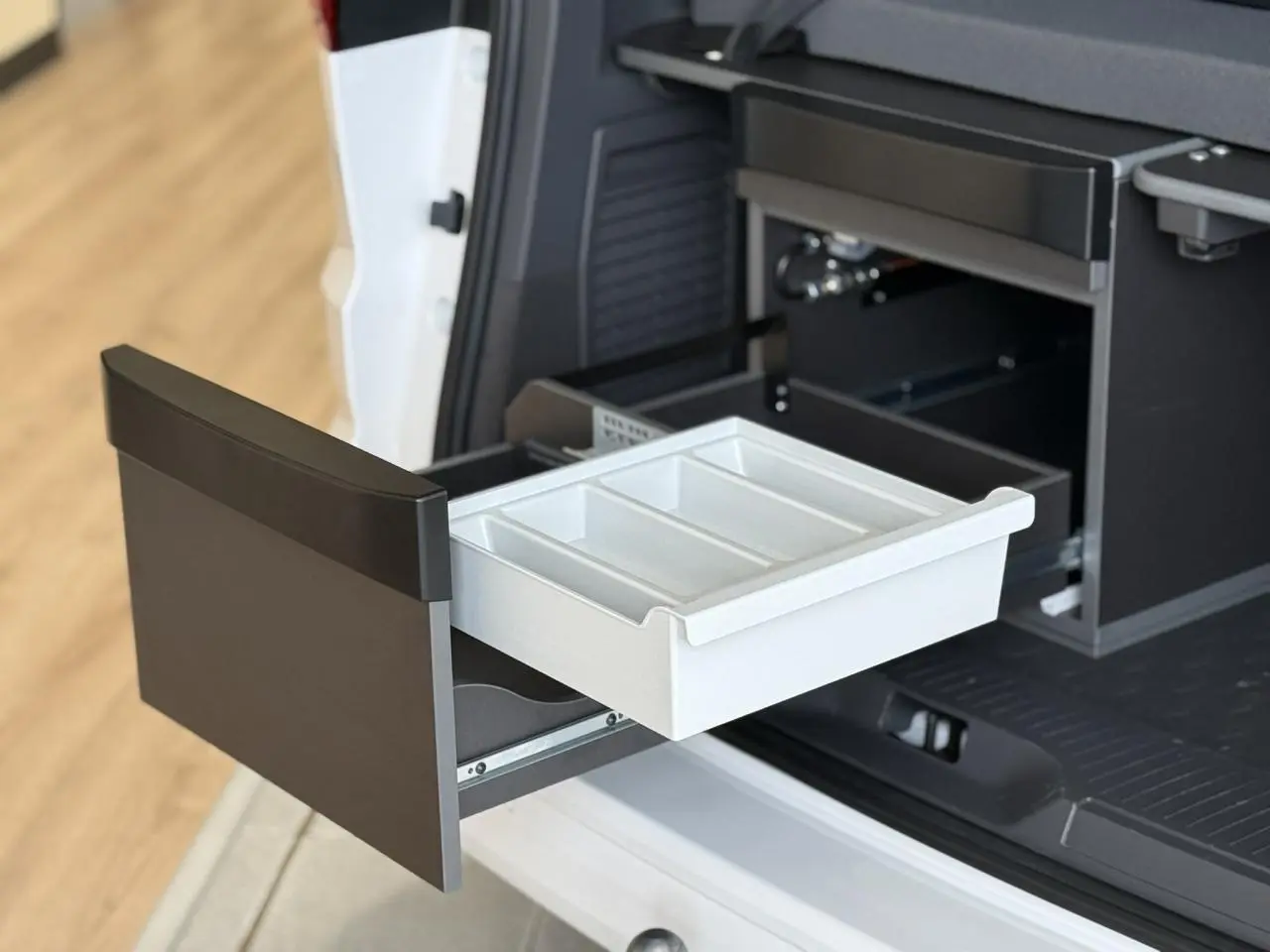 Tiroir de rangement ouvert à l'arrière côté droit du Volkswagen California T7 blanc, montrant la cuisine intégrée.
