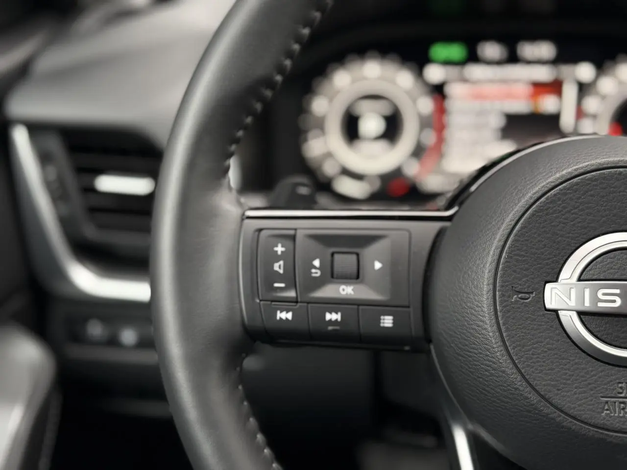 Gros plan sur le volant cuir noir du Nissan Qashqai 2024 avec commandes multifonctions et tableau de bord flou en arrière-plan.