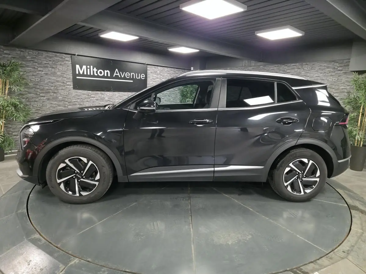 Profil côté gauche du SUV KIA SPORTAGE noir métallisé avec jantes alliage et détails chromés en intérieur showroom.