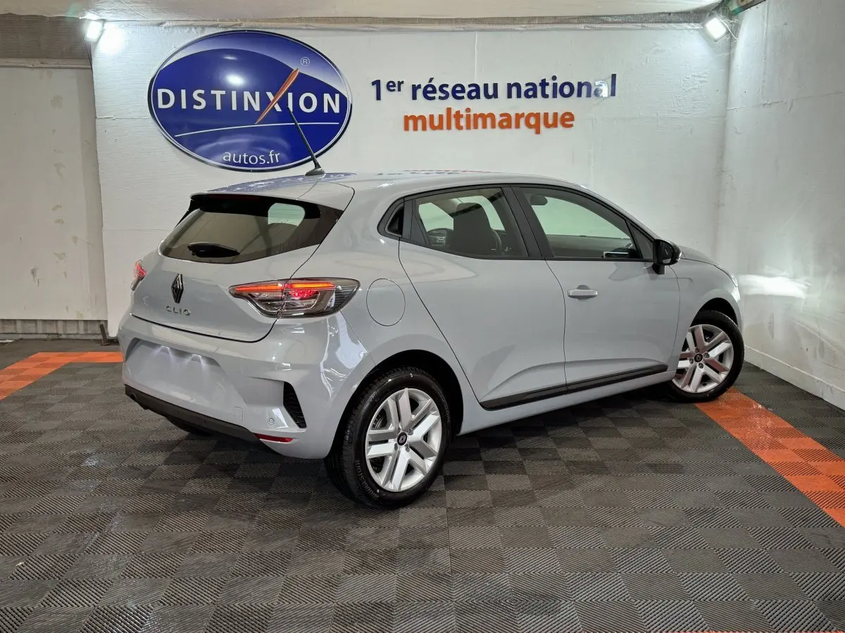 Renault Clio gris clair vue 3/4 arrière droit dans un showroom avec feux arrière allumés et jantes alliage.