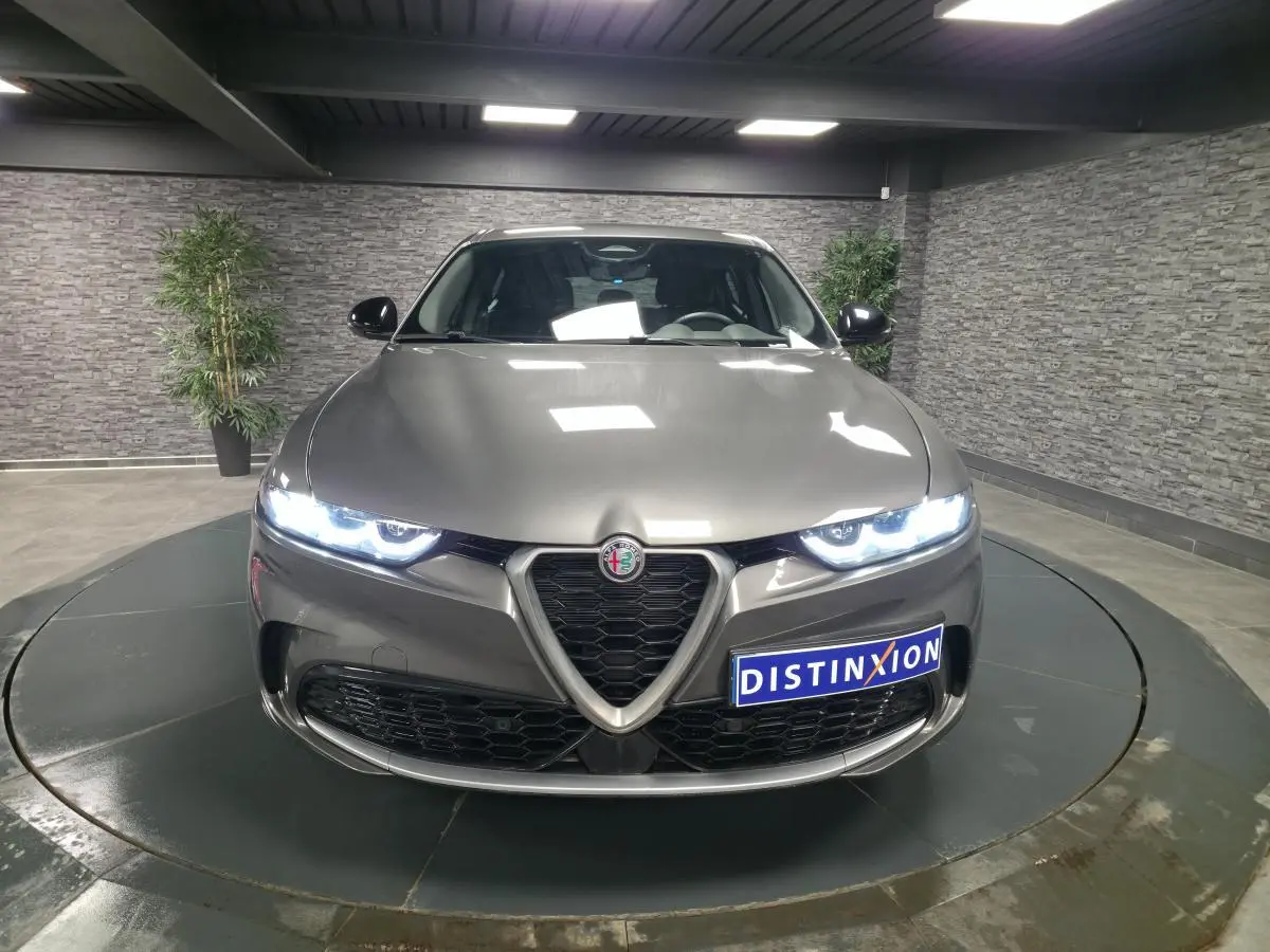 Vue frontale d'une Alfa Romeo Tonale grise métallisée avec phares LED allumés dans un showroom.