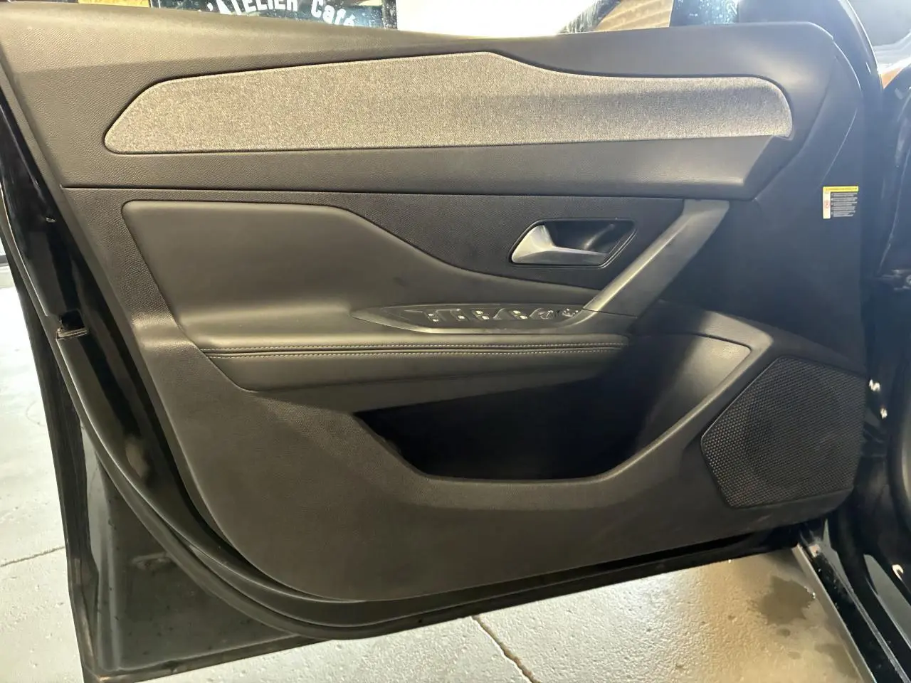 Vue intérieure de la porte avant gauche noire de la Peugeot 308 SW 2024 avec commandes de vitres et haut-parleur intégré.