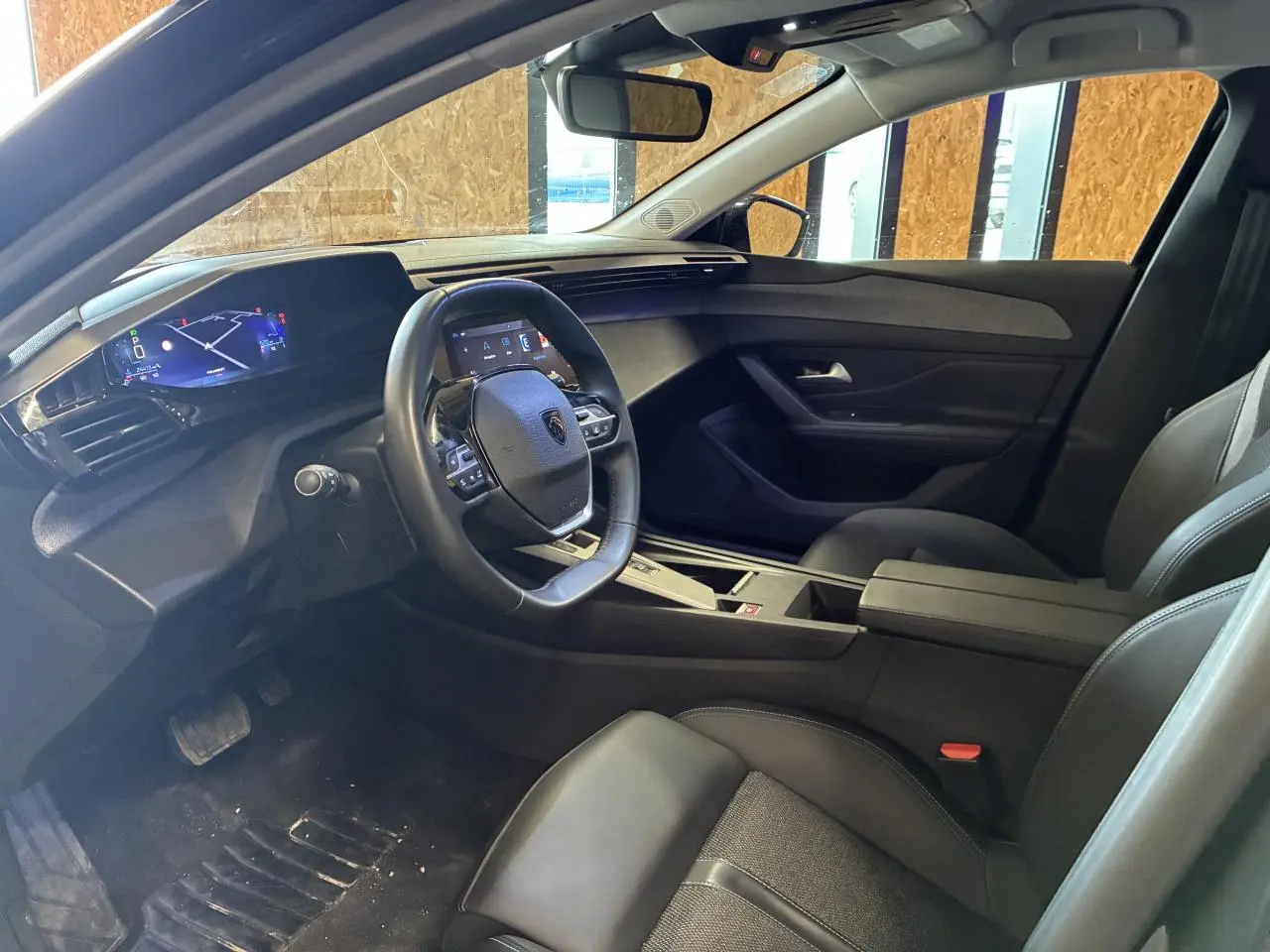 Intérieur de la Peugeot 308 SW 2024 vu côté conducteur, avec tableau de bord numérique et sellerie noire.
