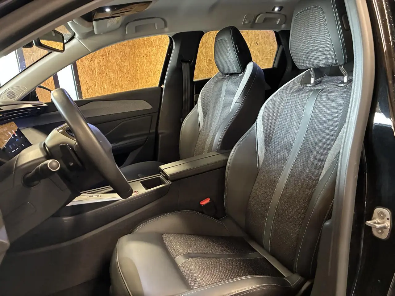 Intérieur avant droit de la Peugeot 308 SW 2024 noire, sièges bi-matière TEP/tissu avec accoudoir central.