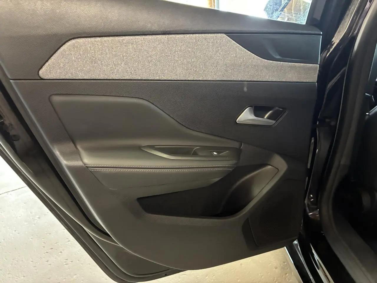 Porte arrière gauche ouverte d’une Peugeot 308 SW noire, montrant le panneau intérieur avec garniture textile et plastique noir.