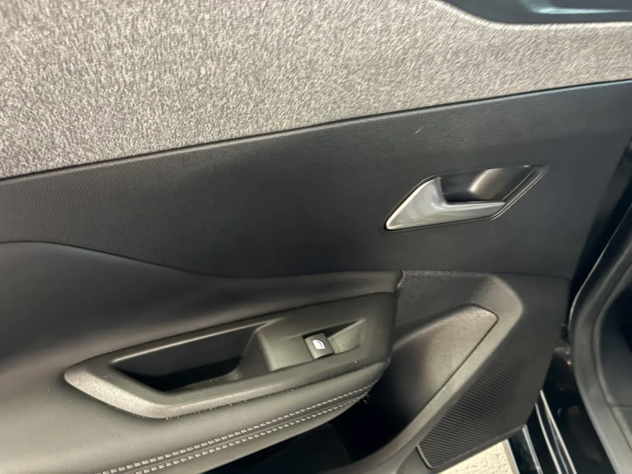 Gros plan sur la porte avant gauche noire du Peugeot 308 SW 2024 avec poignée et commande de vitre électrique.