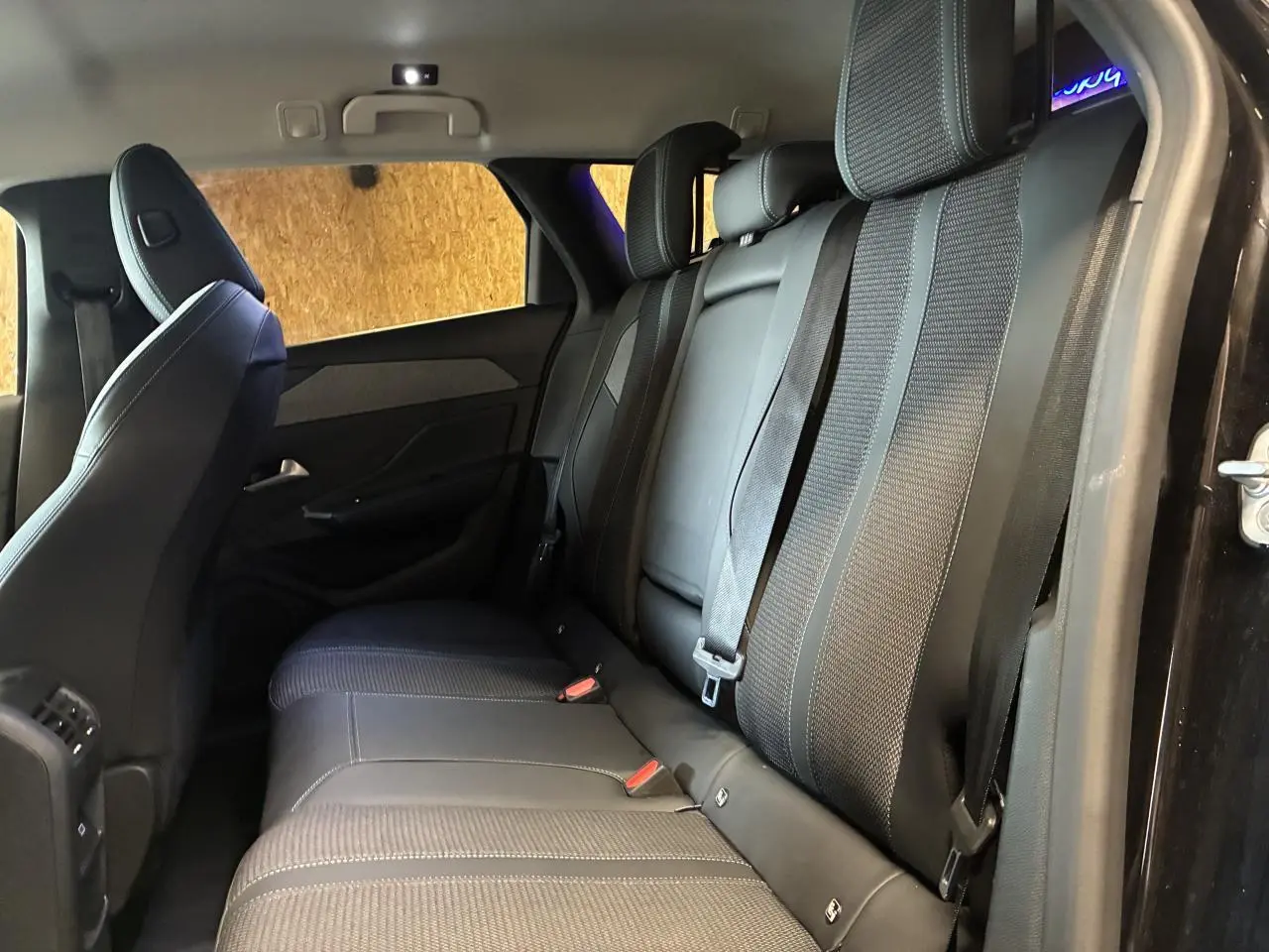 Vue latérale intérieure des sièges arrière noirs en tissu et cuir de la Peugeot 308 SW 2024 avec ceintures attachées.
