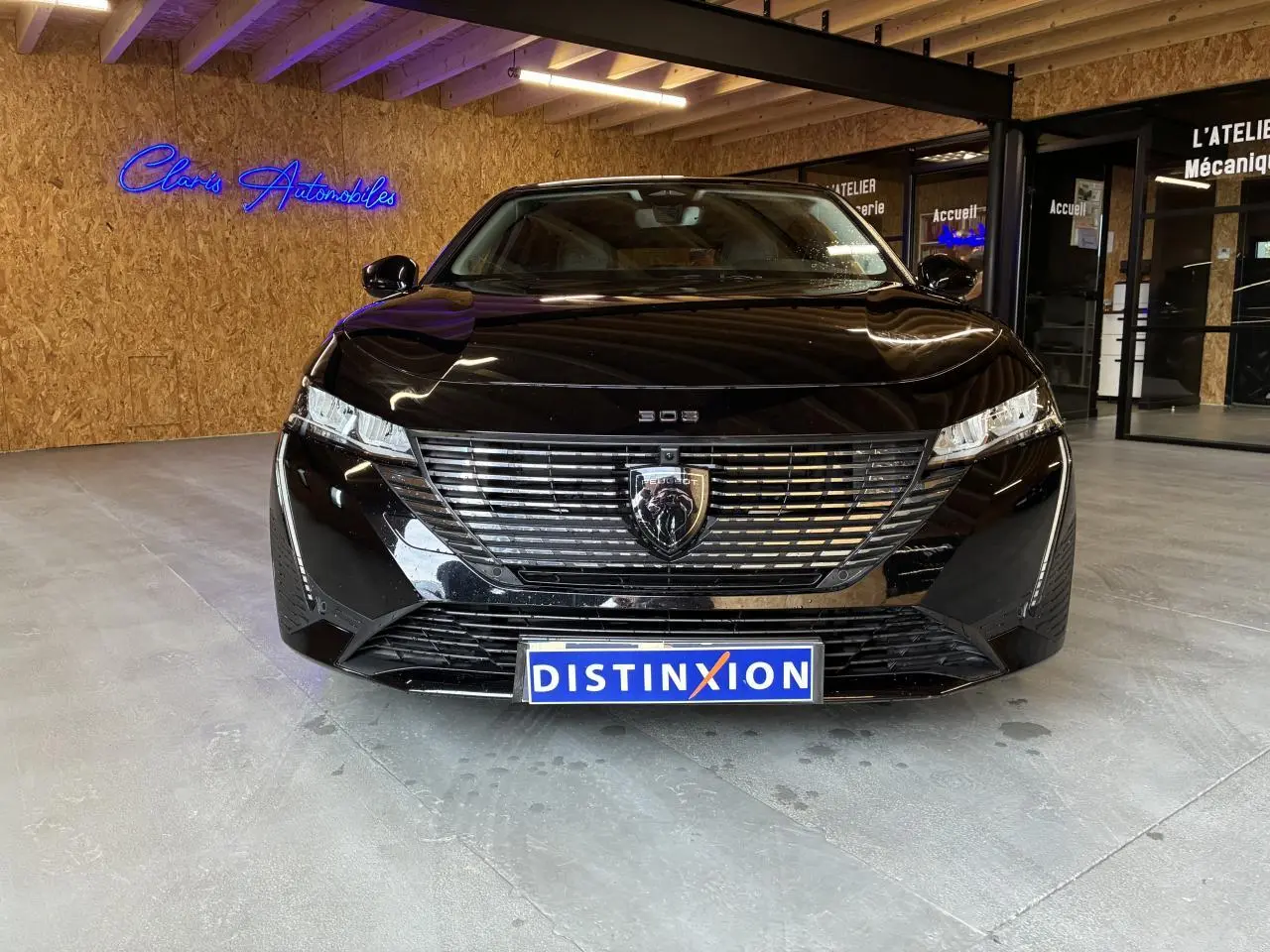 Vue avant d'une Peugeot 308 SW noire 2024 avec calandre noire et logo lion chromé, en intérieur showroom.
