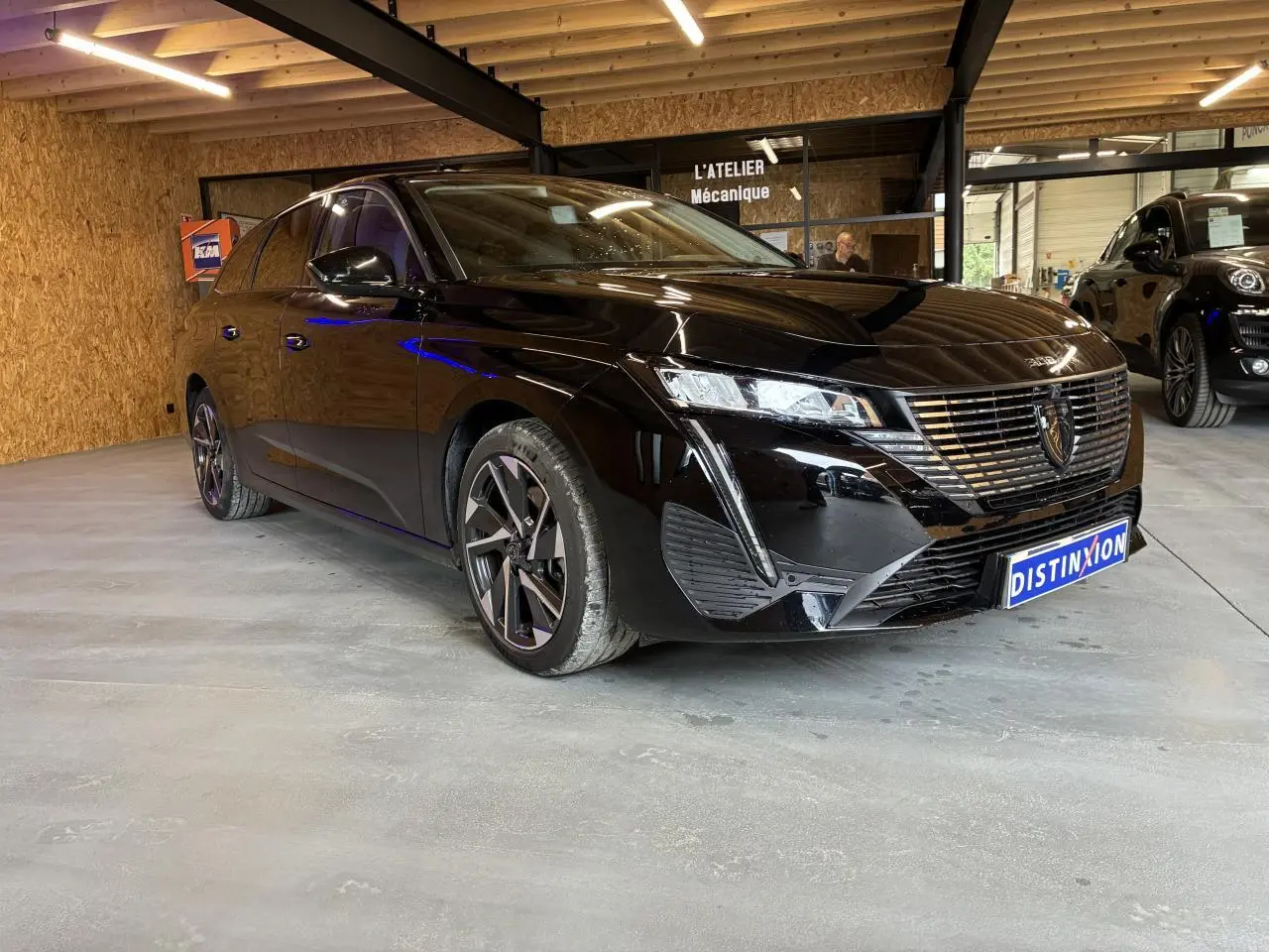 Peugeot 308 SW noire vue 3/4 avant droit en intérieur avec calandre chromée et jantes alliage.
