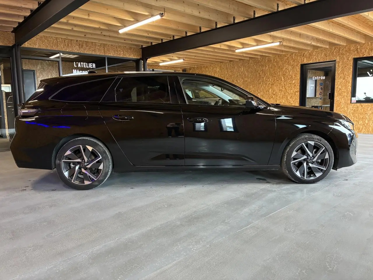 Peugeot 308 SW noire vue de profil côté gauche dans un garage avec jantes alliage et vitres teintées.