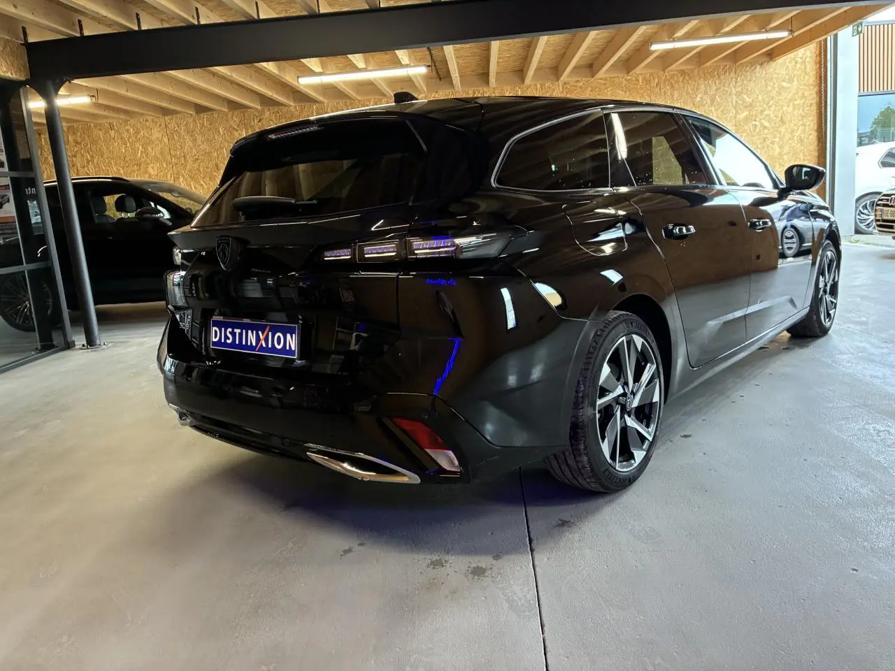 Peugeot 308 SW noire vue 3/4 arrière droit dans un showroom avec feux arrière LED et jantes alliage.