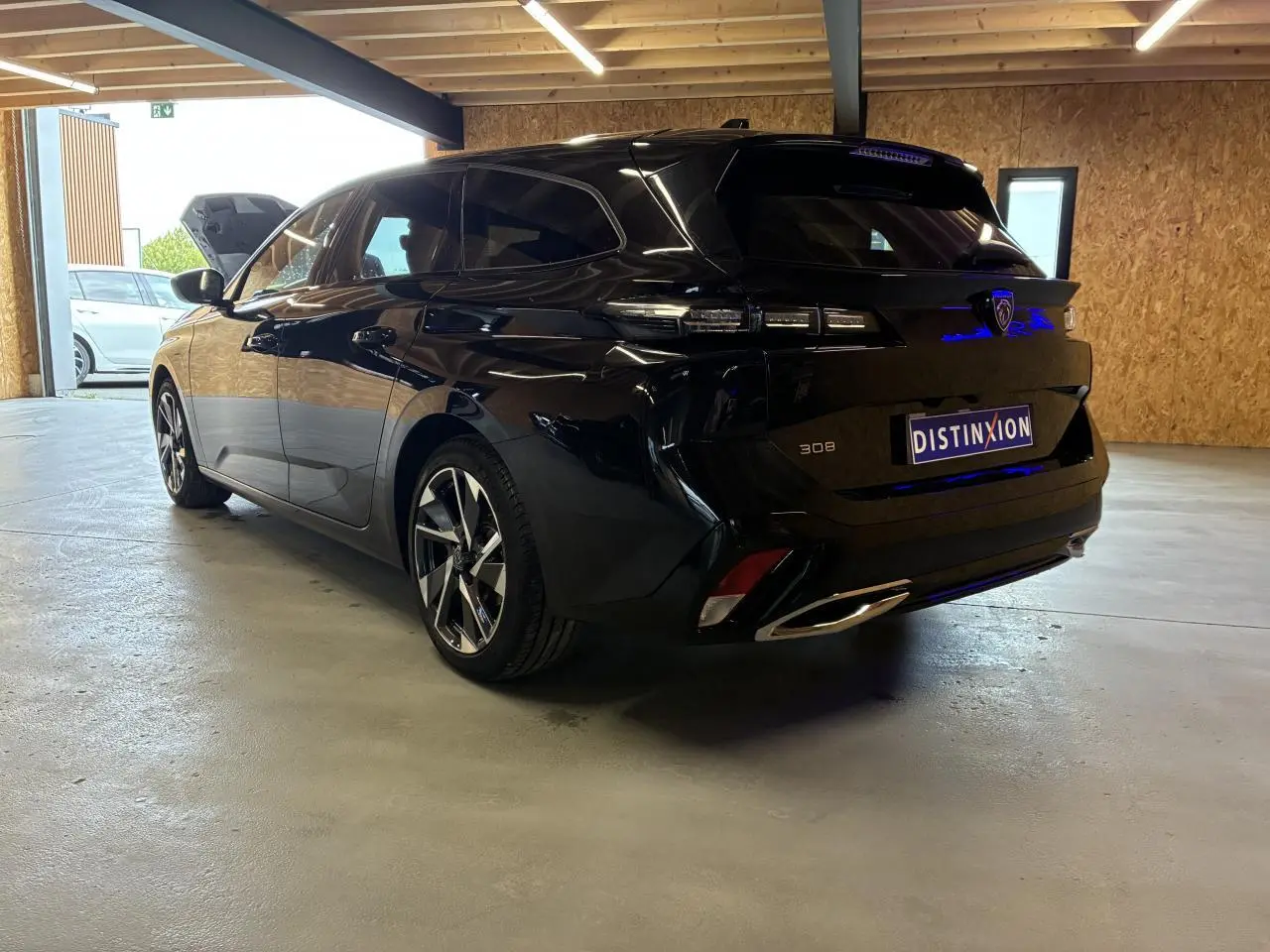 Peugeot 308 SW noire vue 3/4 arrière droit en intérieur, avec jantes alliage et feux arrière LED distinctifs.