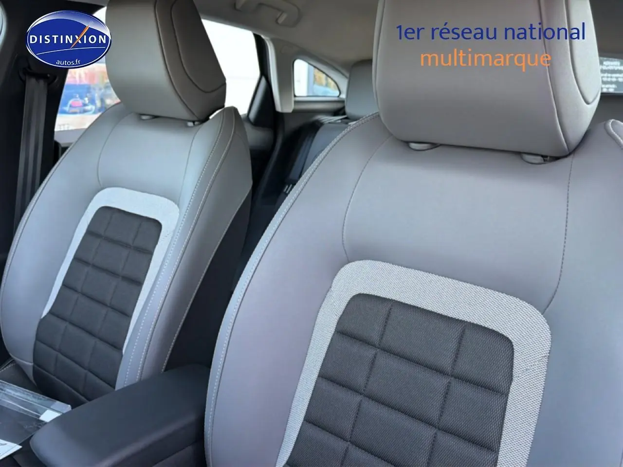 Gros plan sur les sièges avant gris clair et noir de la Citroën C4 électrique 2025 avec accoudoir central.