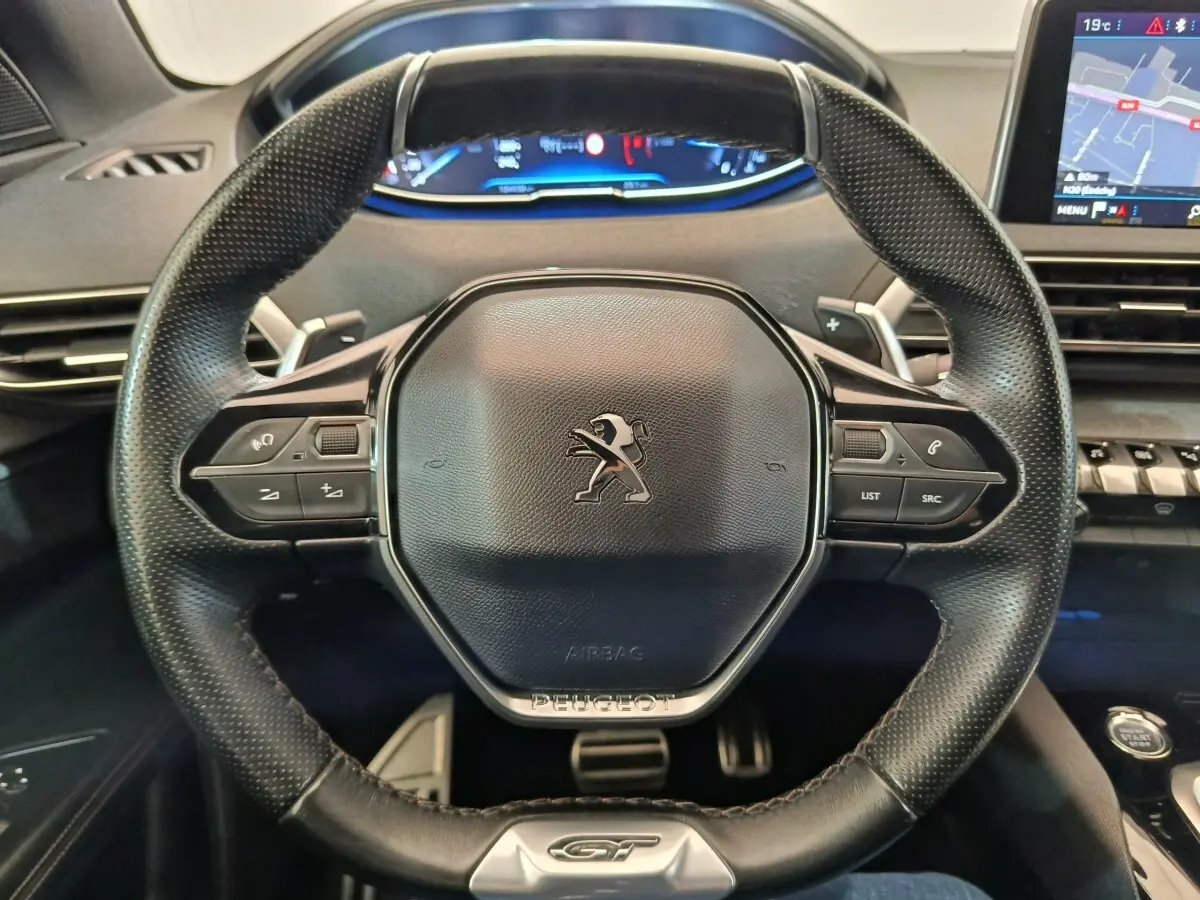 Vue rapprochée du volant cuir perforé noir avec logo Peugeot et tableau de bord numérique du 5008 GT gris clair.
