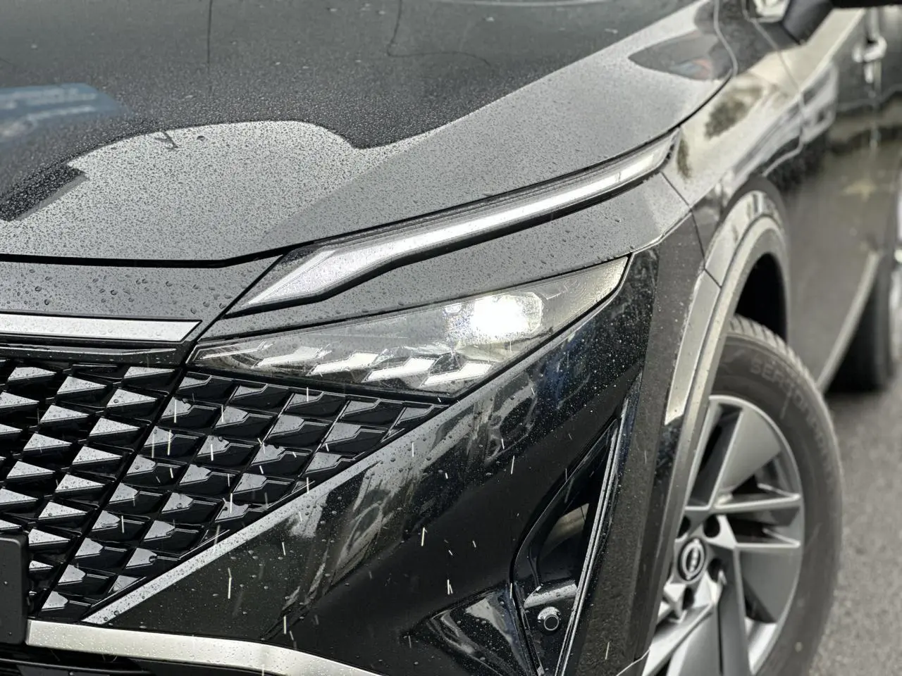 Gros plan sur l'avant droit du Nissan Qashqai noir nacré 2025, mettant en valeur le phare LED et la calandre texturée.