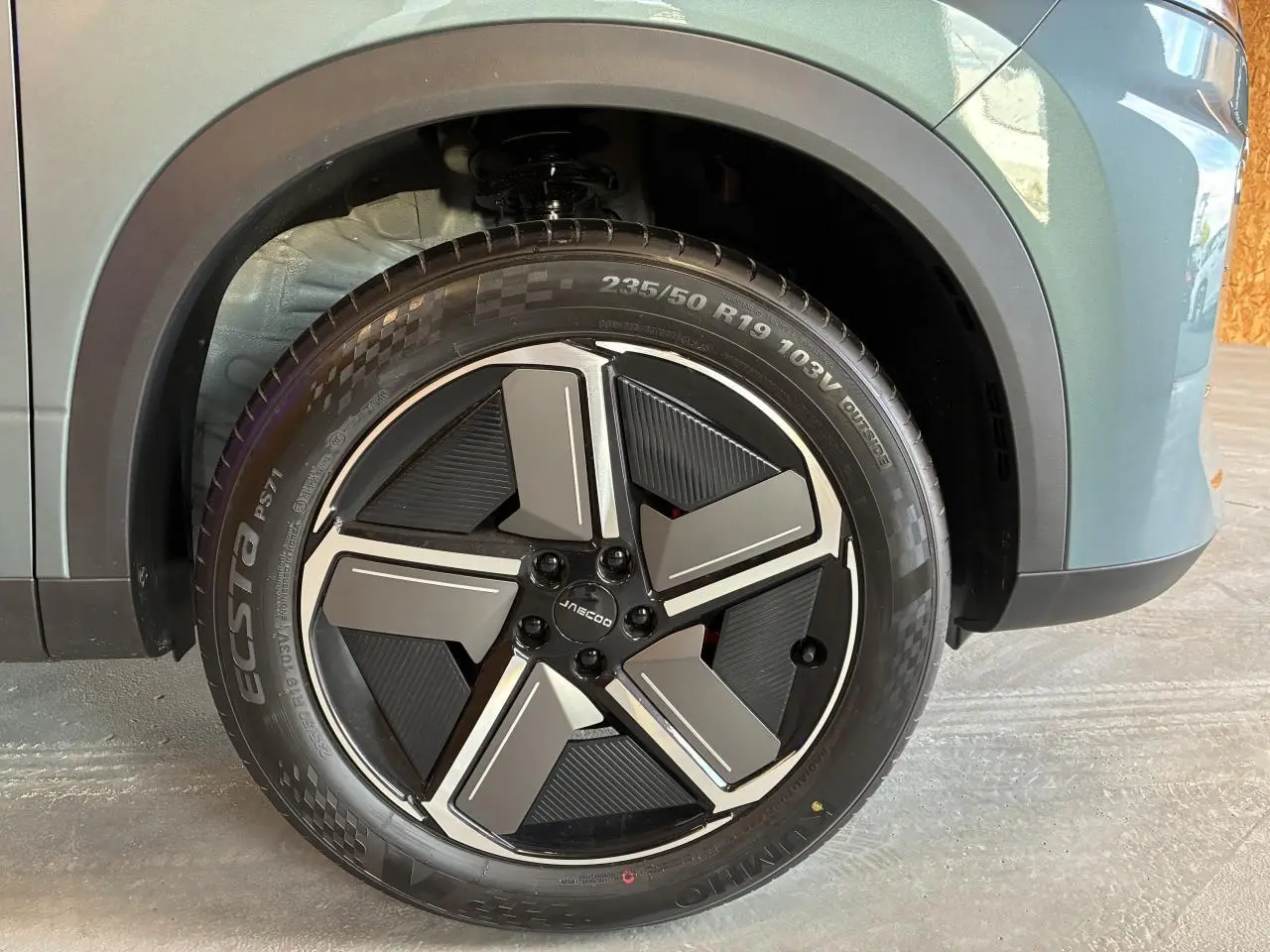 Gros plan sur la jante alliage 19 pouces noire et grise du SUV JAECOO J7 gris olive, avec logo central visible.