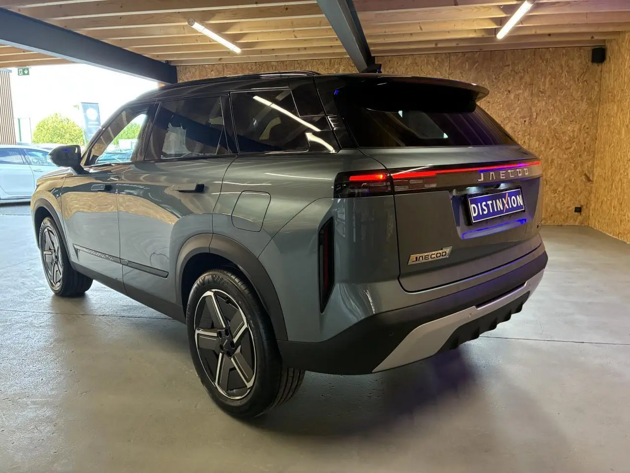 Vue 3/4 arrière droite du SUV JAECOO J7 gris olive avec toit noir et feux arrière LED allumés en intérieur.