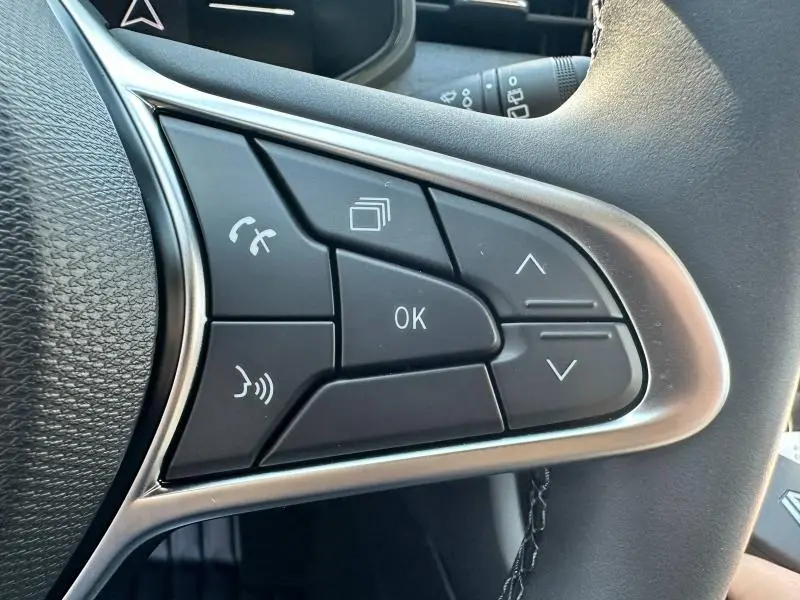 Gros plan sur les commandes multifonctions noires du volant de la Renault Clio Gris Rafale, boutons de navigation et appel.
