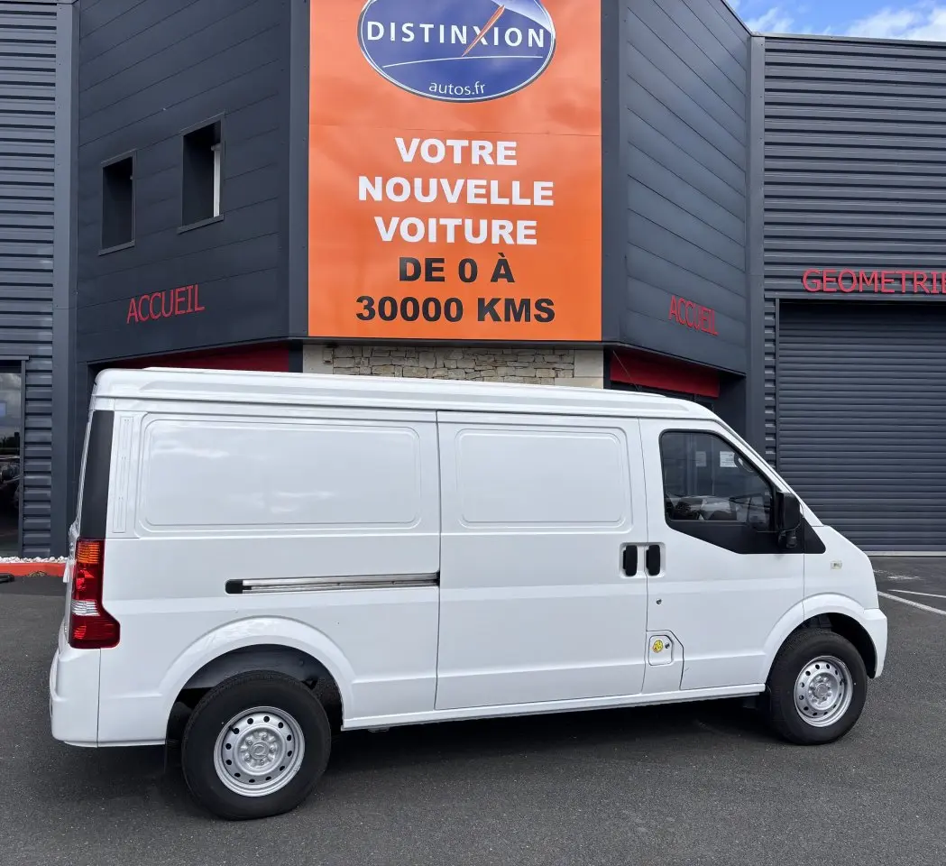 Profil latéral droit du fourgon blanc DFSK EC35 BEV 39KWH, sans fenêtres latérales, garé devant un bâtiment commercial.